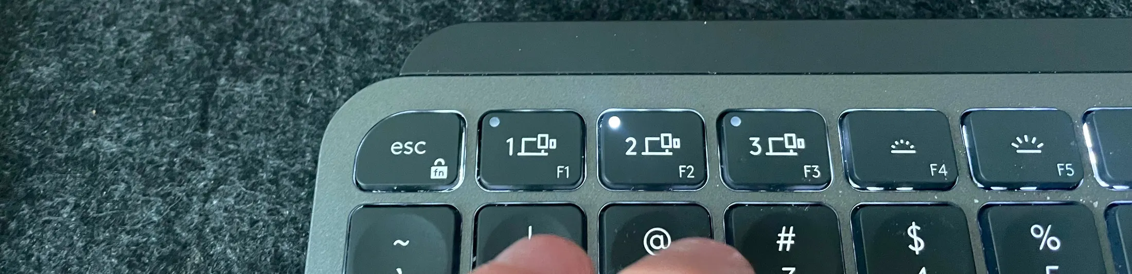 A finger reaching for the host-2 key on an MX Keys Mini keyboard, its indicator light lit.